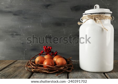 Milk can with eggs on wooden table and dark background
