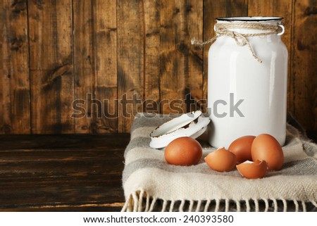 Milk can with eggs and eggshell on rustic wooden background
