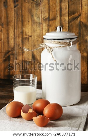 Milk can with eggs, eggshell and glass on rustic wooden background