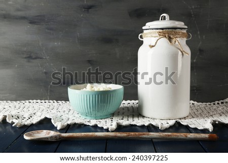 Milk can with bowl of cottage cheese on lace doily on wooden table and dark background
