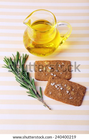 Crispbread with salt, jug of oil and sprigs of rosemary on cutting board, on striped background