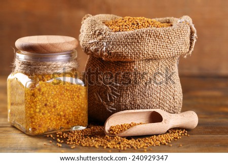 Mustard seeds in bag and Dijon mustard in glass jar on wooden background