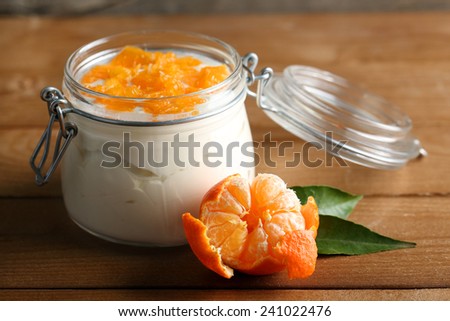 Tasty milk dessert with fresh tangerine pieces in glass jar, on  wooden background