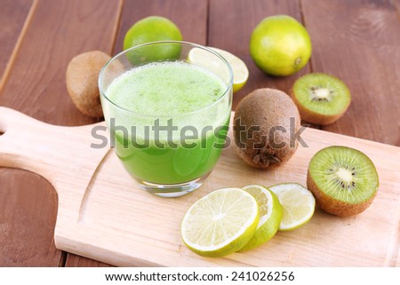 Glass of fresh lime juice with pieces of lime and kiwi on cut board and wooden table background