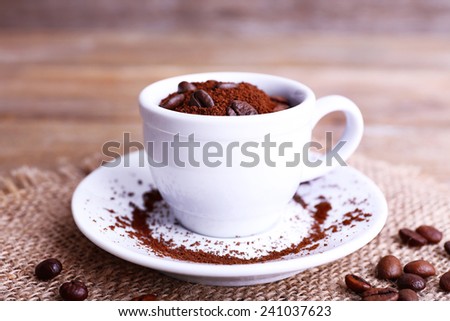 Mug of coffee beans and ground coffee on sackcloth on wooden table on wooden  background