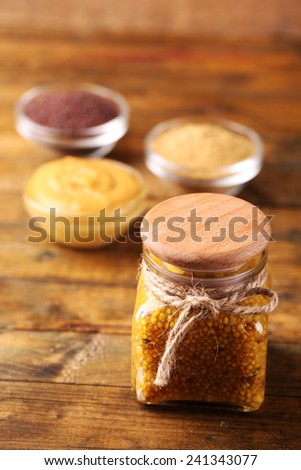 Dijon Mustard in glass jar  and mustard seeds and sauce in bowls on wooden background
