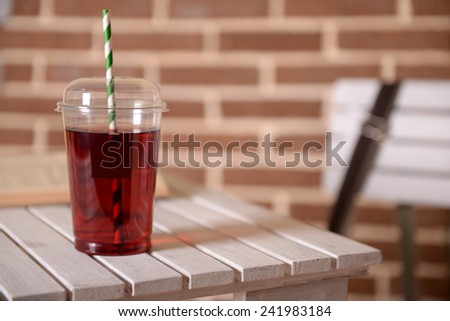 Pomegranate juice in fast food closed cup with tube and book on wooden table and brick wall background