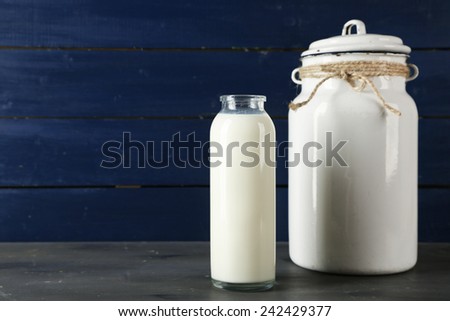 Milk can and glass bottle on color wooden background