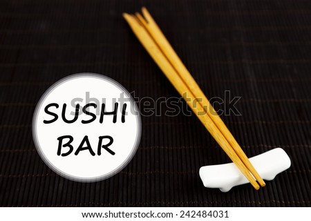 Pair of chopsticks and Sushi Bar text on black bamboo mat background