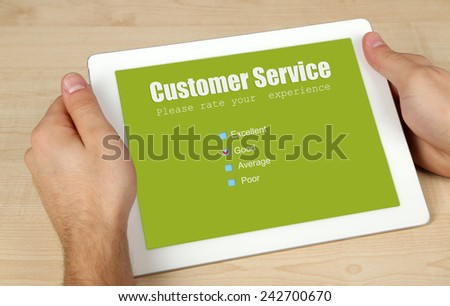 Hands holding tablet PC with Customer Service text on screen on wooden table background