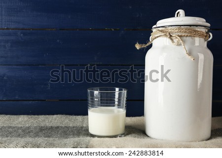 Milk can and glass on color wooden background