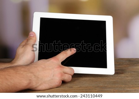 Hands holding tablet PC on wooden table and light blurred background
