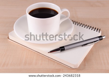 Cup of coffee on saucer with notebook and pen on wooden table background