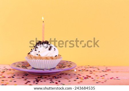Birthday cup cake with candles on plate on color wooden table and orange background
