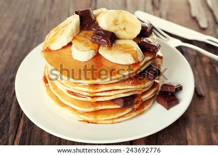 Stack of delicious pancakes with chocolate, honey and slices of banana on plate on wooden table background