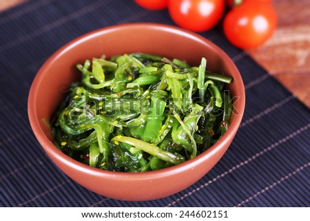 Seaweed salad in bowl with cherry tomatoes on bamboo mat background