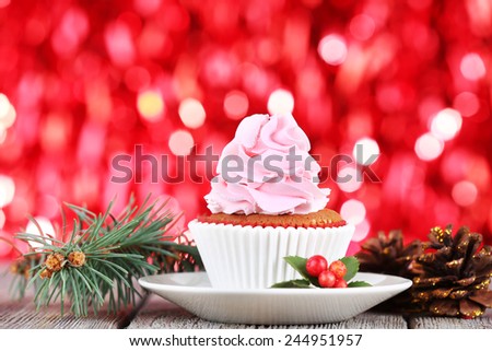 Cup-cake with cream on saucer and Christmas decoration on wooden table and shine brightly background