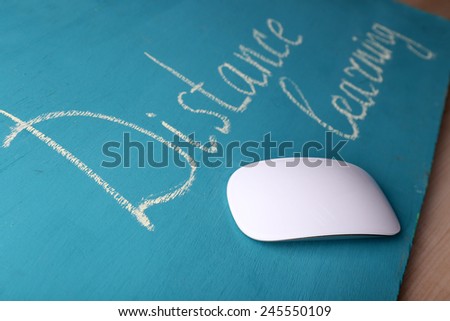 Computer mouse and inscription Distance Learning on blackboard on wooden table background