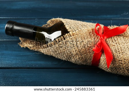 Wine bottle wrapped in burlap cloth on color wooden planks background