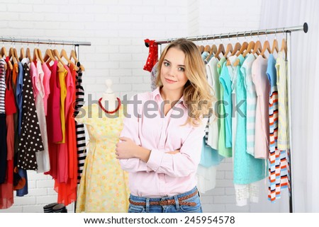 Beautiful young stylist near rack with hangers