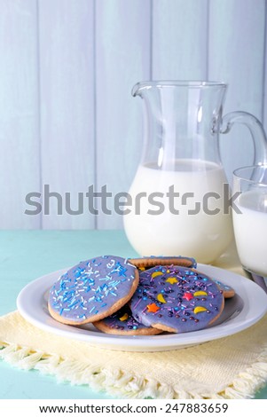 Glazed cookies with glass and jug of milk on color wooden background