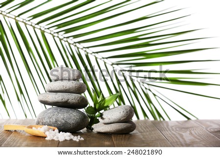 Stack of spa stones with spoon of sea salt on wooden surface isolated on white