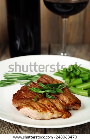 Steak with herbs on plate and bottle of wine on wooden table