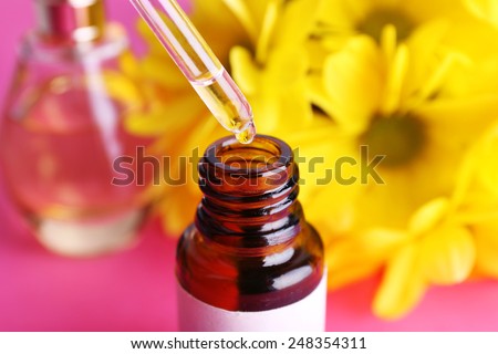 Dropper bottle of perfume with yellow chamomile on pink background