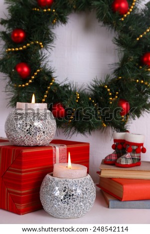 Christmas decoration with wreath, candles and present boxes on shelf on white wall background