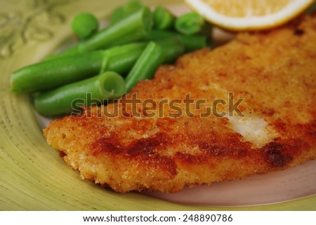 Breaded fried fish fillet and potatoes with asparagus and sliced lemon on green plate background