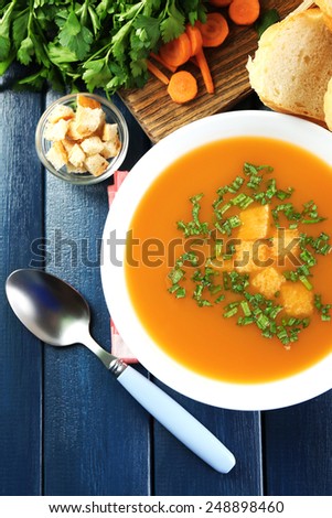 Composition with carrot soup, ingredients and herbs on color wooden background