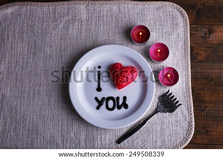 Cookie in form of heart on plate with inscription I Love You, and candles on napkin and wooden table background