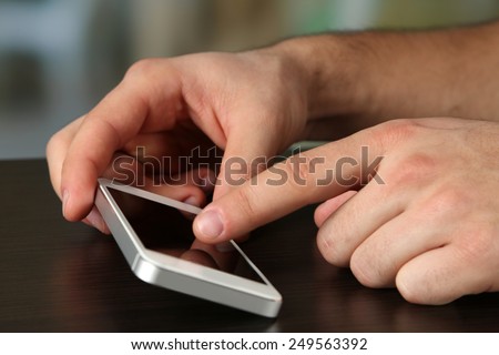 Hands holding smart mobile phone on wooden table and light blurred background