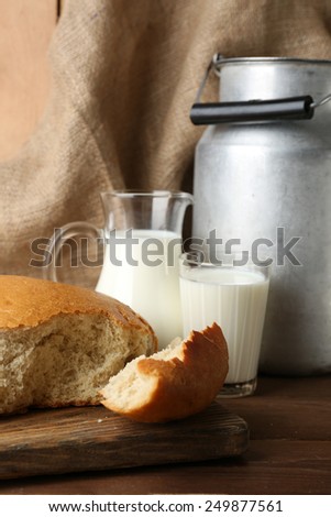 Retro can for milk with fresh bread and glass of milk on wooden background. Bio products concept