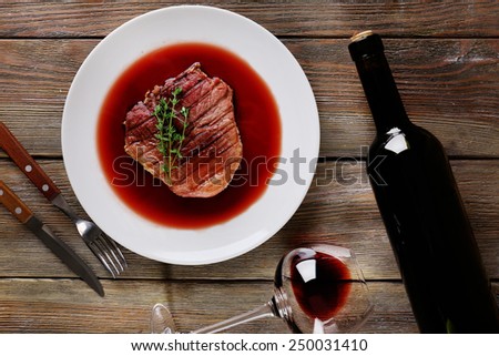Grilled steak in wine sauce with bottle of wine on wooden background