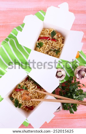 Chinese noodles and sticks in takeaway boxes on green napkin on pink background