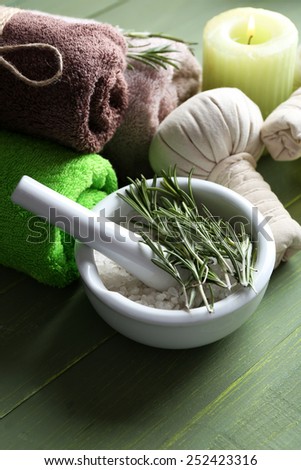 Branches of rosemary and sea salt in bowl, towels, candle and bottle with massage oil on color wooden background. Rosemary spa concept
