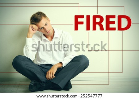 Sad fired office worker sitting on floor on wall background