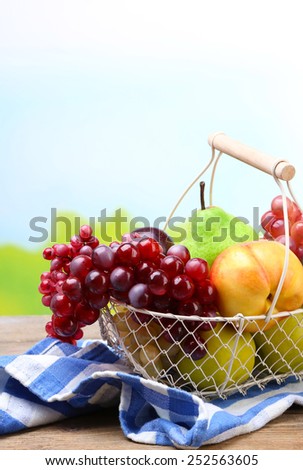 Assortment of juicy fruits in wicker basket on table, on bright background