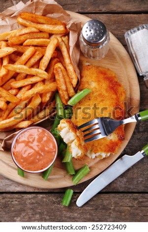 Breaded fried fish fillet and potatoes with asparagus and sauce on cutting board and rustic wooden background