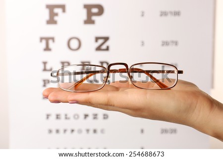 Eye glasses in female hand on eyesight test chart background