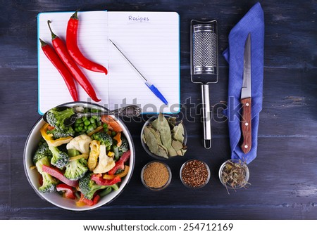 Frozen vegetables and blank notebook, on wooden table background