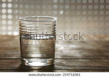 Glass of clean mineral water on wooden surface and lattice background