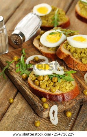 Sandwiches with green peas paste and boiled egg with onion rings and lemon on wooden planks background