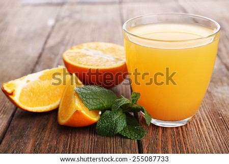 Glass of orange juice with oranges on wooden table close up