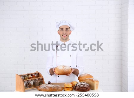 Baker in kitchen at table with freshly loaves of bread on white brick wall background