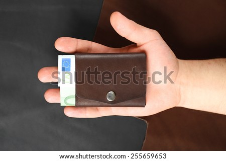Man holding hand made leather wallet with money on black background