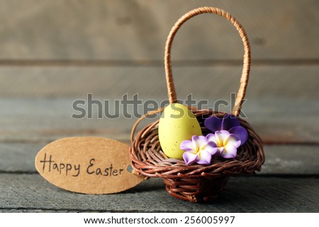 Bird egg in wicker basket with decorative flowers on wooden background