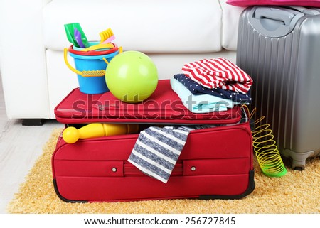 Suitcases packed with clothes and child toys on fur rug and white sofa background