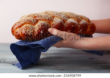 Loaf of freshly bread in female hands with napkin on color wooden table and light background